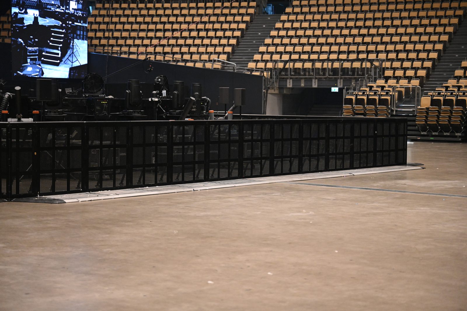 Absperrbarriere vor der Bühne einer leeren Arena, dahinter Tribünen; die freie Innenfläche bestimmt die Besucherkapazität