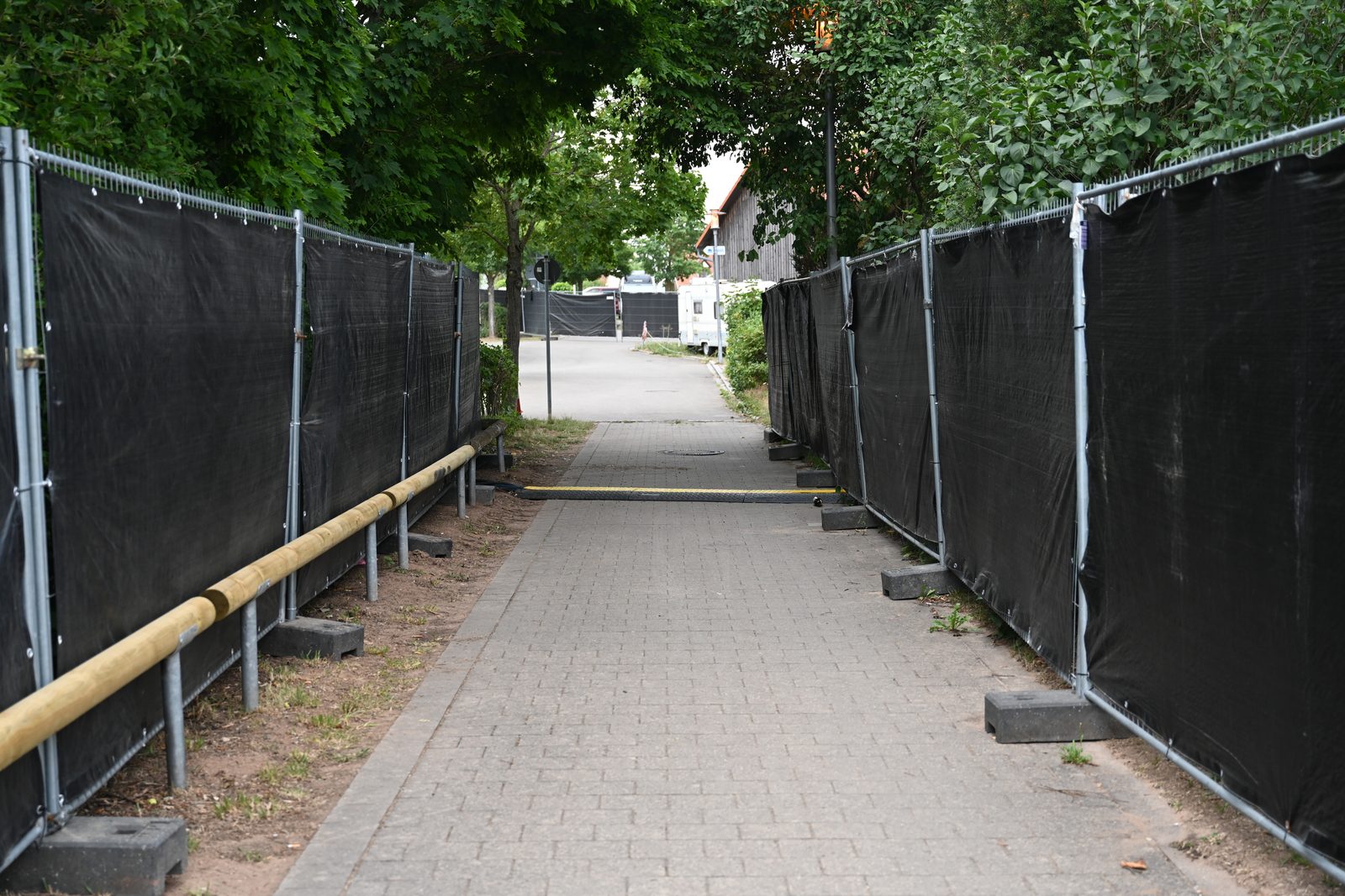 Mobilzaun mit schwarzer Sichtblende bildet einen Gang entlang eines Gehwegs, quer eine Kabelbrücke