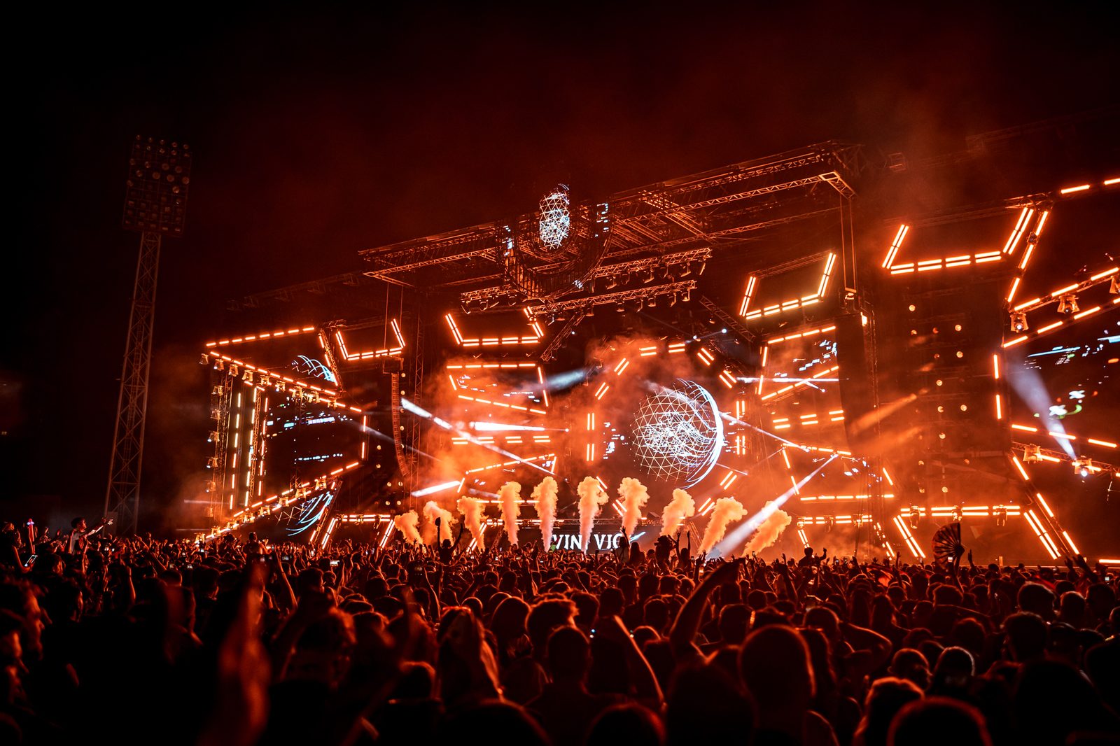 Dichtes Publikum vor der beleuchteten Hauptbühne eines Festivals bei Nacht mit Flammeneffekten