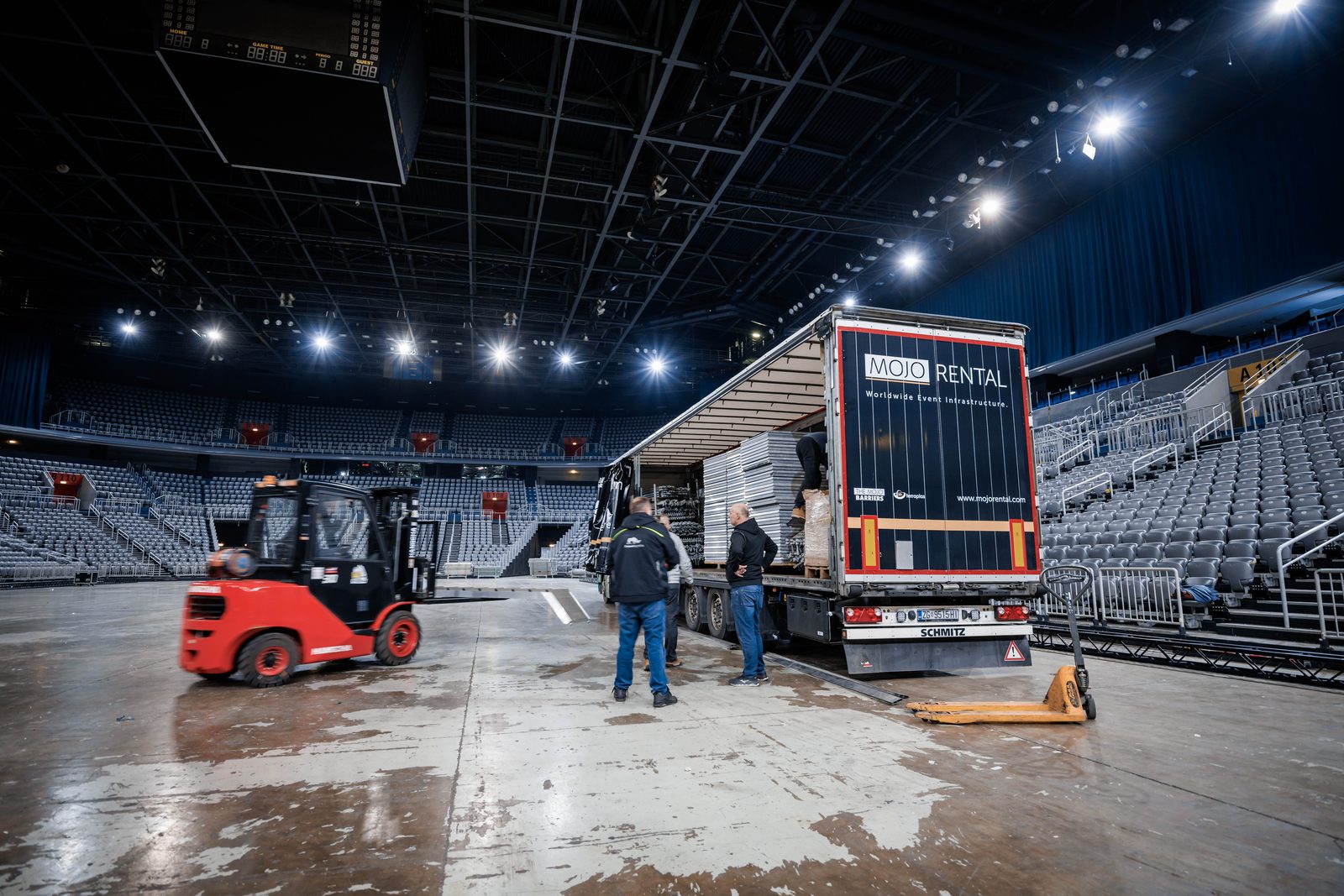 Eventlogistik in der Arena: Crew entlädt Absperrgitter und Bodenplatten mit Gabelstapler und Hubwagen aus dem Sattelzug