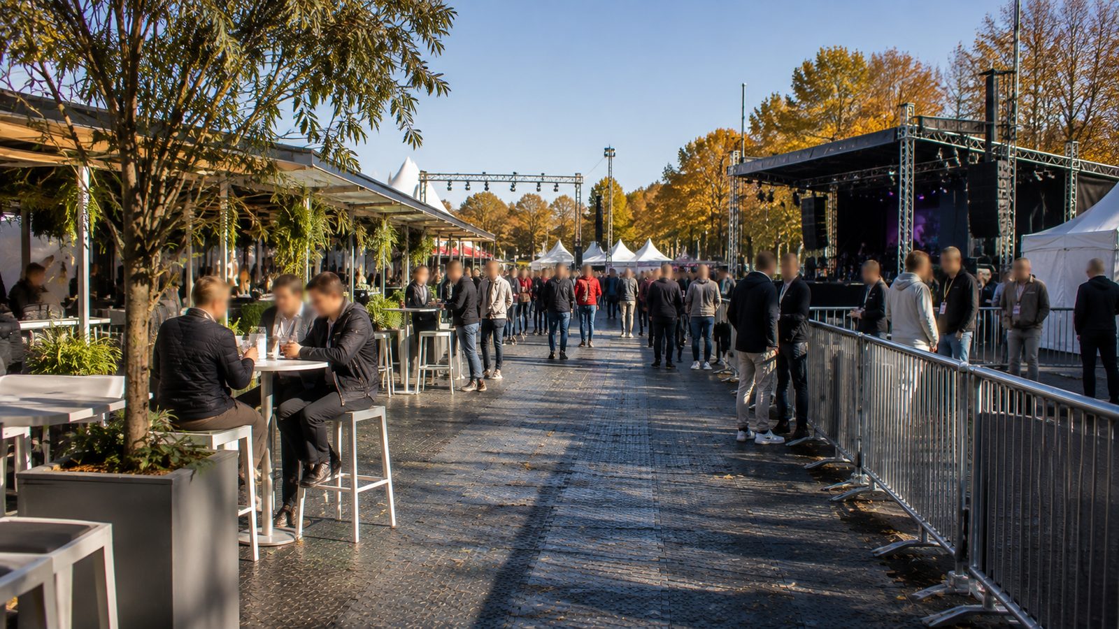 Besucher auf einem befestigten Fahrweg aus Bodenplatten zwischen Barrieren und Stehtischen bei einem Open-Air-Event