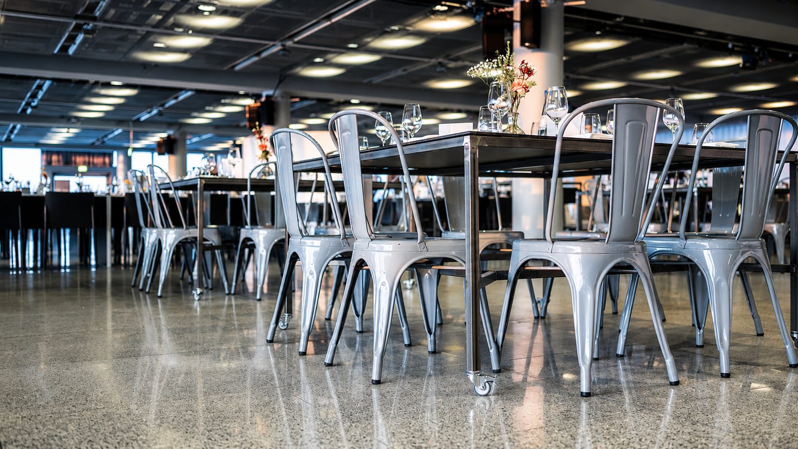 Reihe silbergrauer Metallstühle an schmalen Rolltischen mit Weingläsern und kleinen Blumenvasen