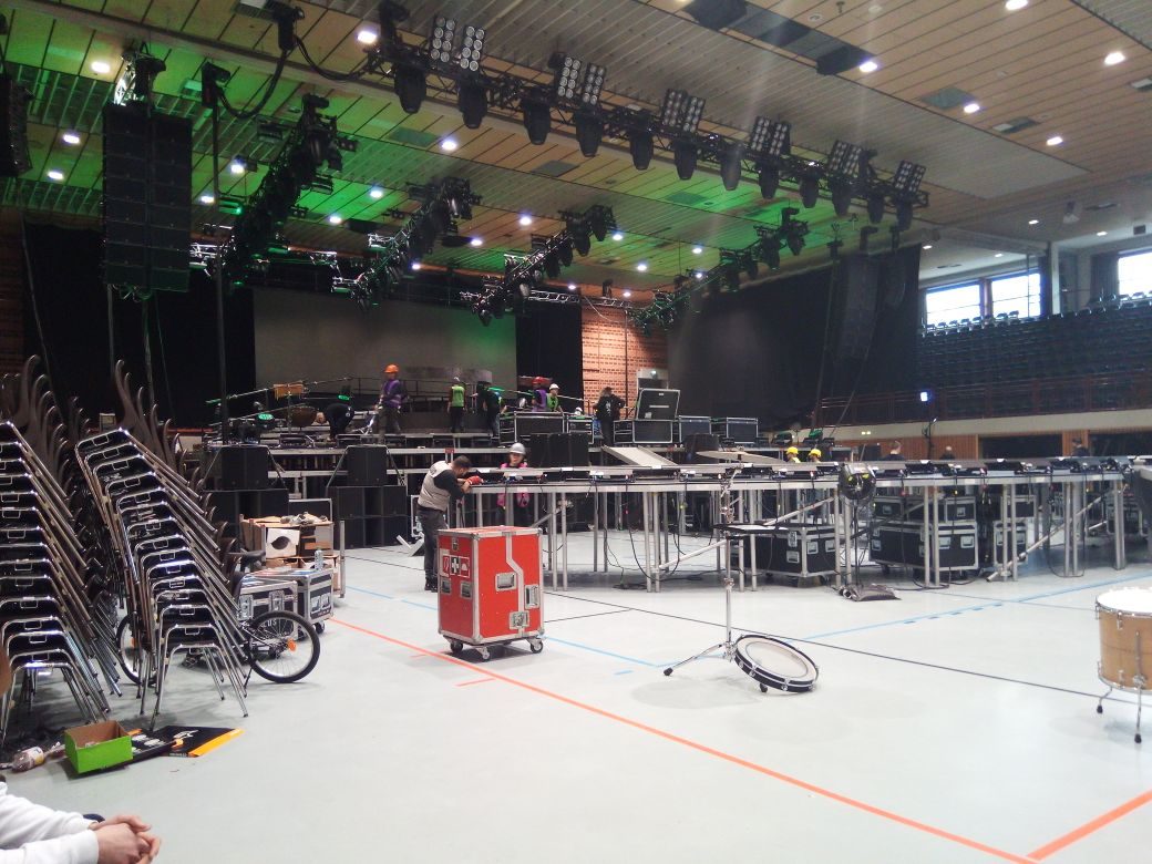 Changeover in einer Mehrzweckhalle: Stapelstühle, ein rotes Flightcase und Podesterie auf einem Sporthallenboden