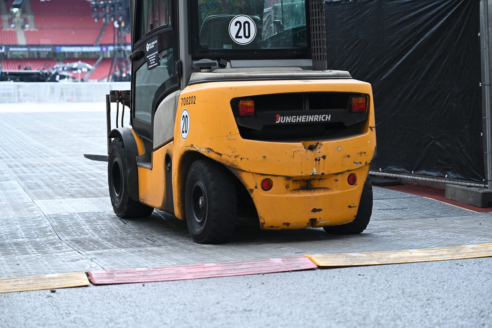 Flächenlast: Gabelstapler fährt über ein Bodenplattenfeld im Stadion, im Hintergrund leere rote Sitzreihen