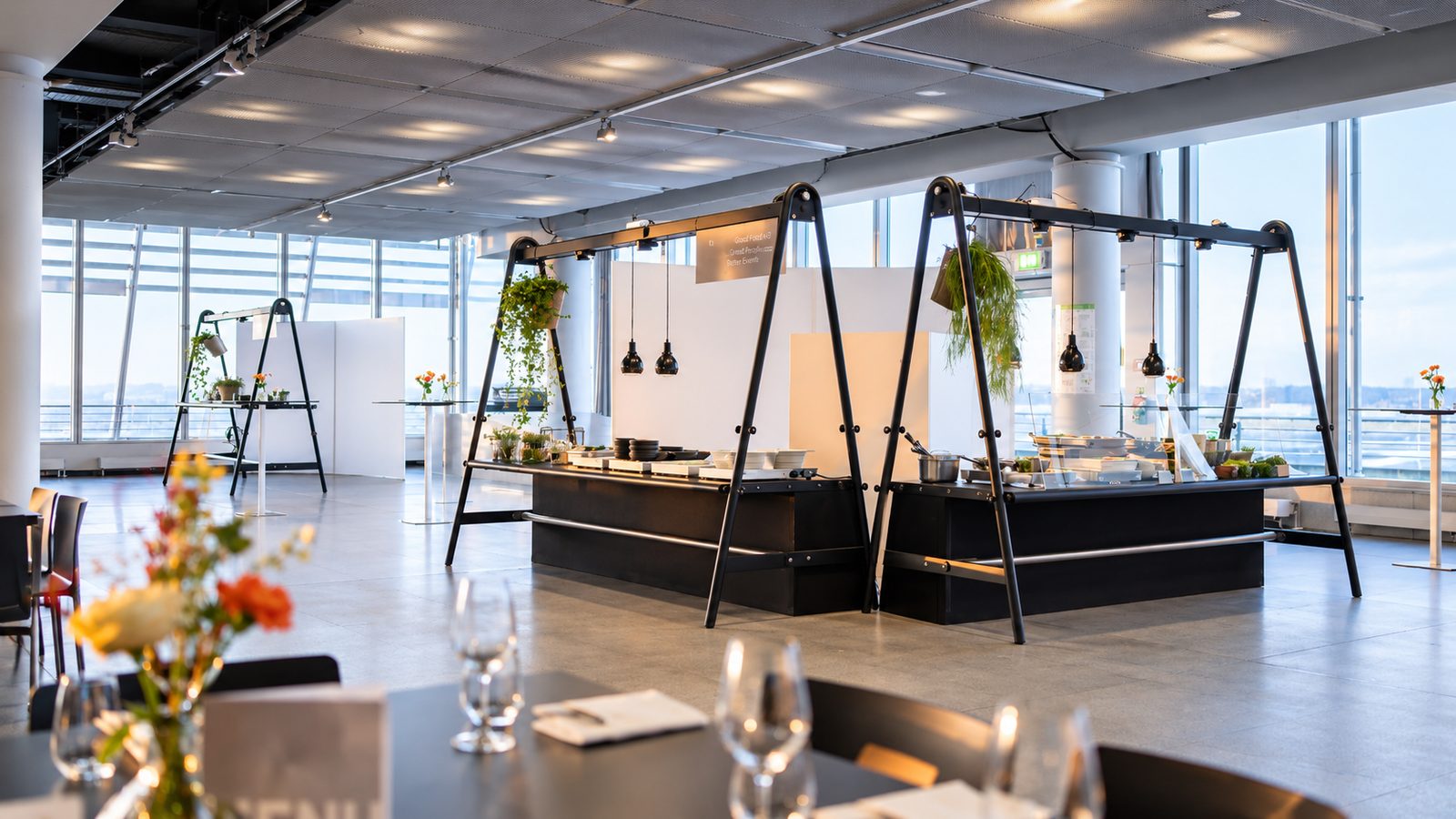 Eventlocation mit raumhoher Glasfassade: zwei schwarze Catering-Theken unter Rahmengestellen mit Pendelleuchten