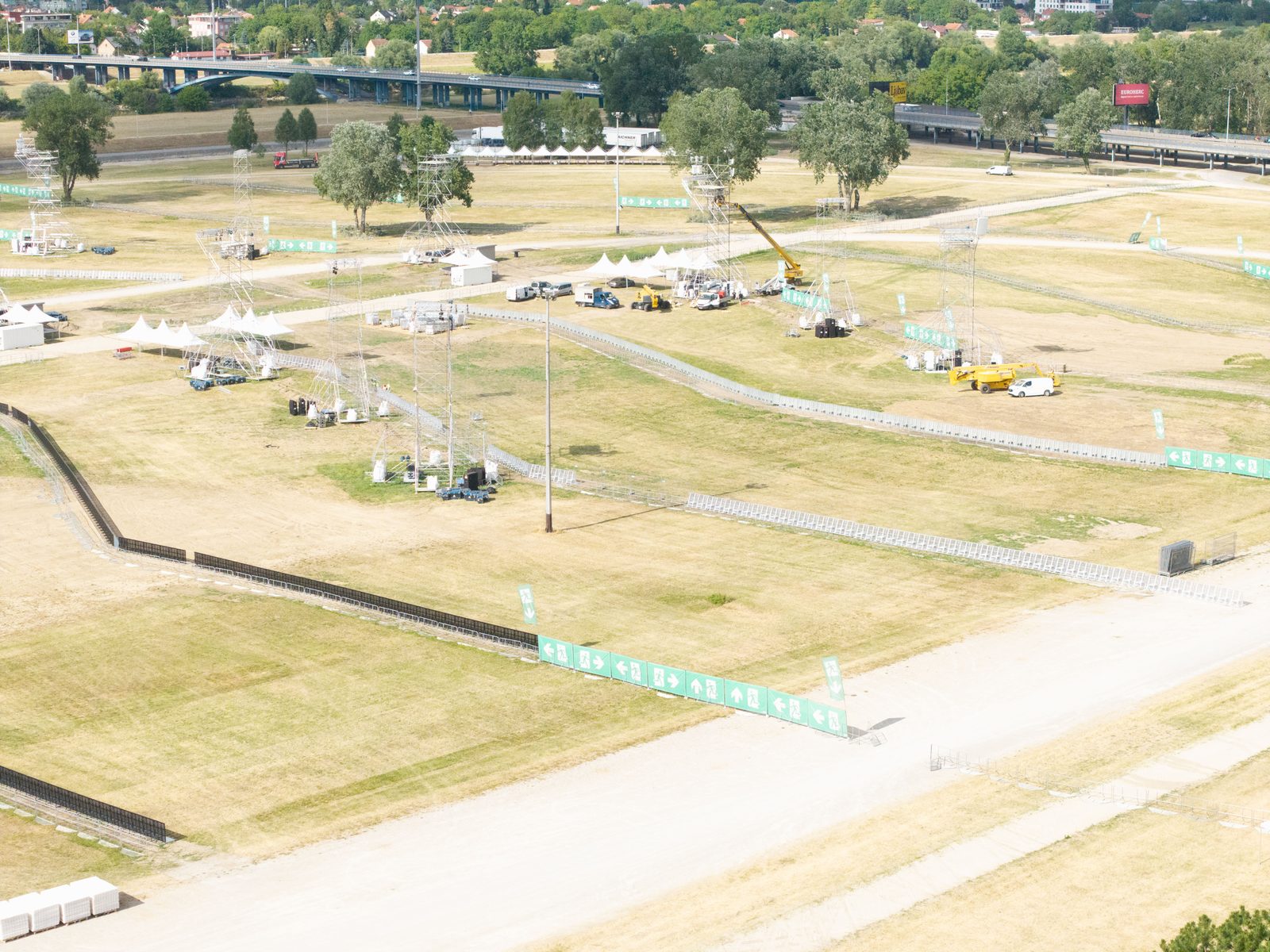 Festivalplanung im Aufbau: Luftbild eines Geländes mit Gerüsttürmen, Absperrgittern und türkisen Leitbannern