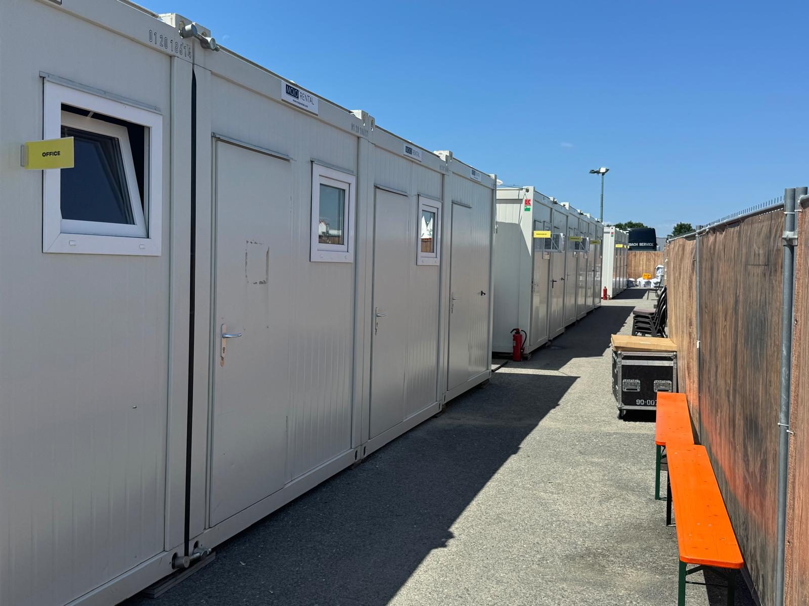Gasse zwischen zwei Reihen weißer Bürocontainer mit gelbem OFFICE-Schild und Feuerlöscher auf dem Festivalgelände