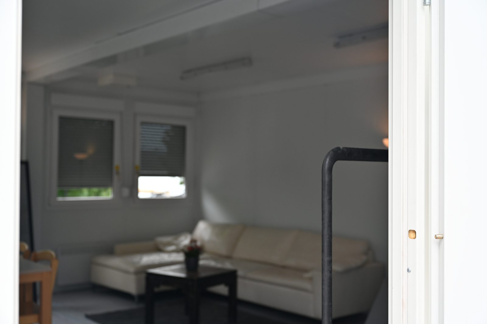 Blick durch die offene Containertür auf helle Ledercouch, Couchtisch und Fenster mit Plissee-Rollos