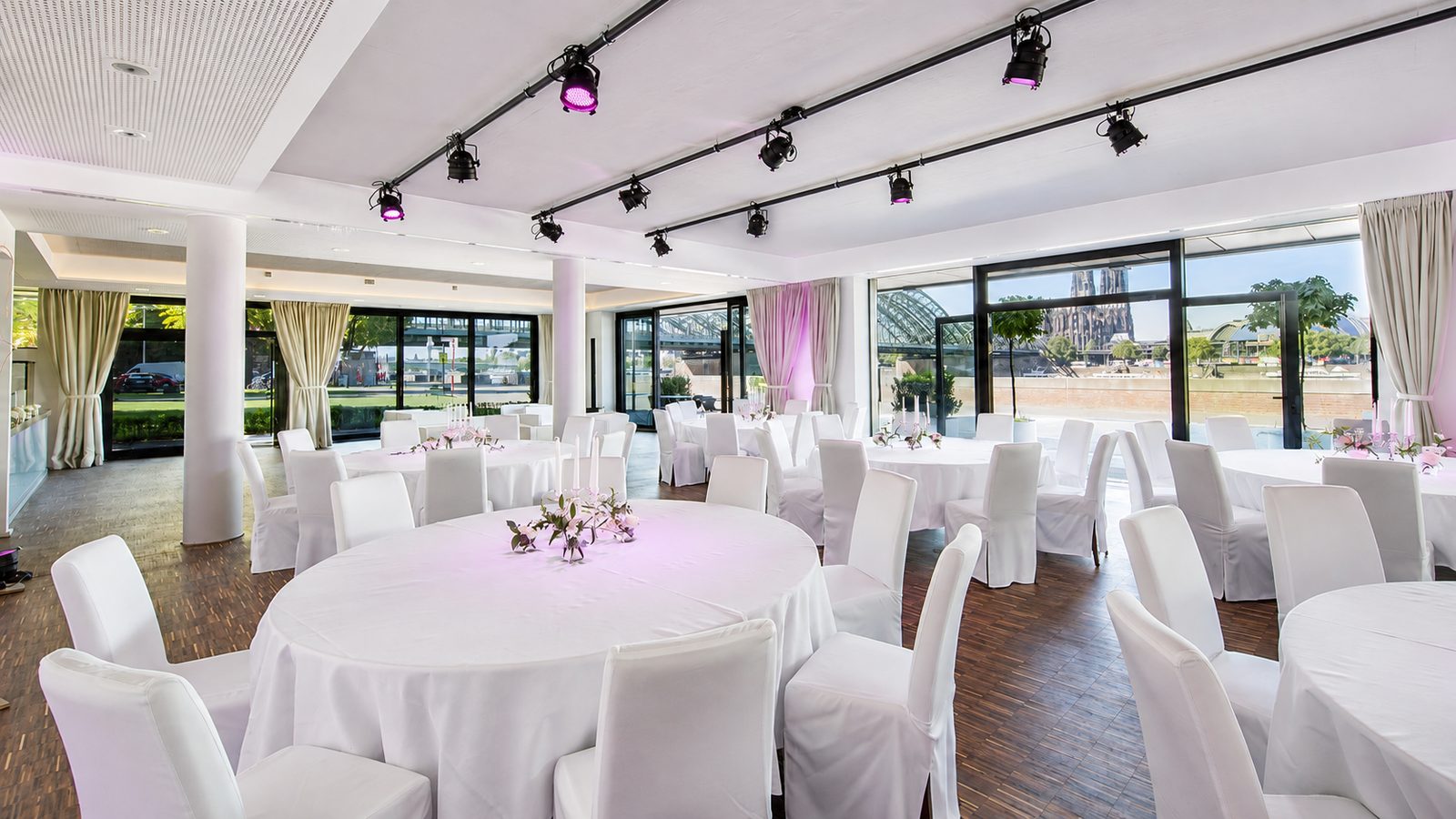 Hospitality bei Veranstaltungen: eingedeckte Rundtische mit weißen Stuhlhussen im Saal, Blick auf Dom und Rhein
