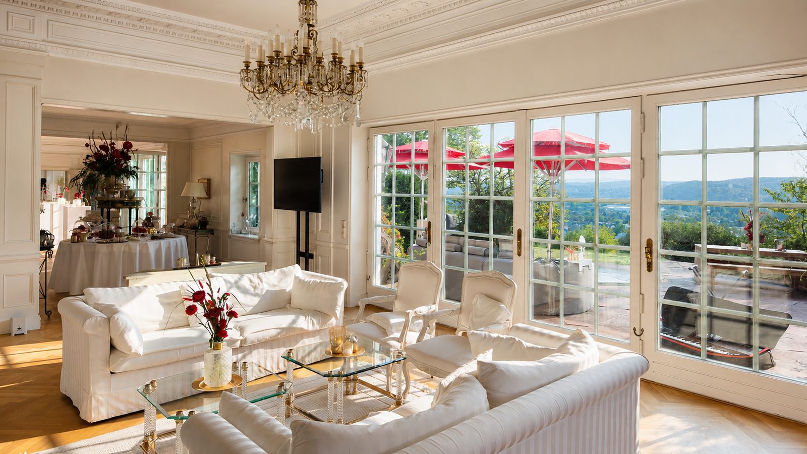Klassizistischer Salon mit weißen Polstersofas, Kronleuchter und Sprossentüren zur Terrasse