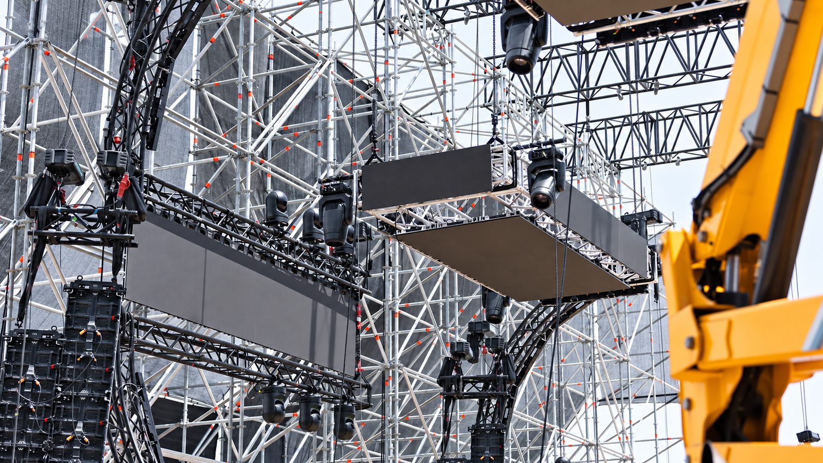 Gerüstturm mit orangefarbenen Rohrkappen, daran hängende LED-Wandmodule und schwarze Moving-Head-Scheinwerfer