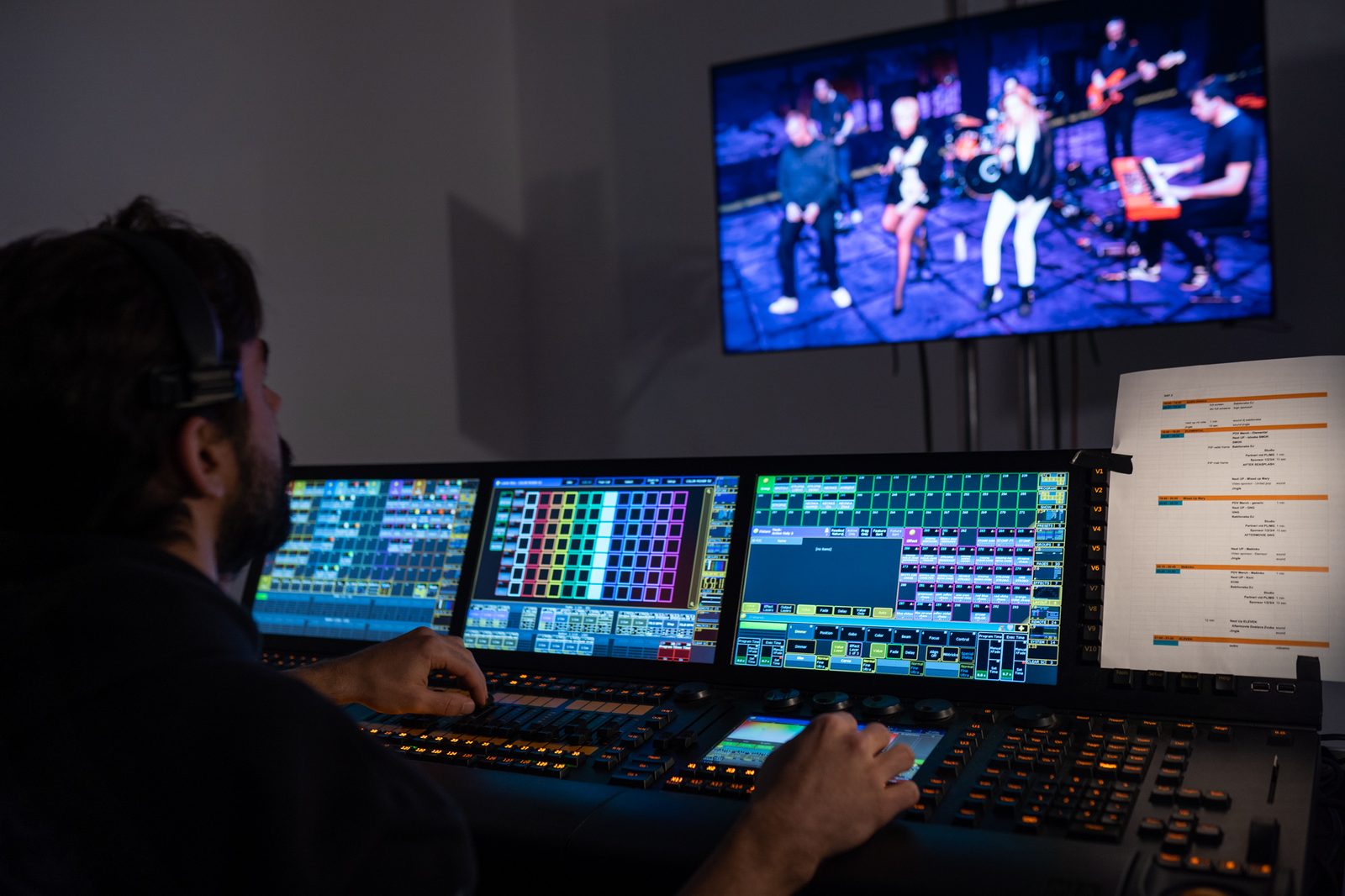 Techniker am Lichtpult mit mehreren Touchscreens, auf dem Monitor die Bühne mit einer Band