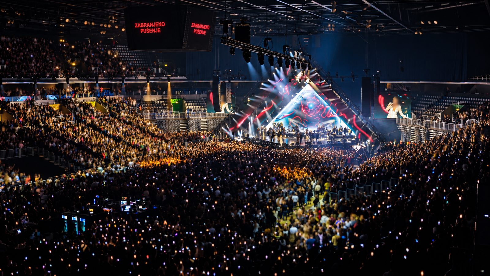 Arena-Totale vom Oberrang: Orchester auf der Bühne, Videowände seitlich, Publikum mit Handylichtern