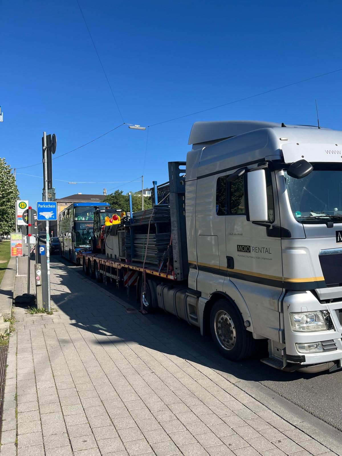 Silberner Sattelzug von MOJO Rental mit gestapelten Absperrgittern wartet am Bordstein einer Straße