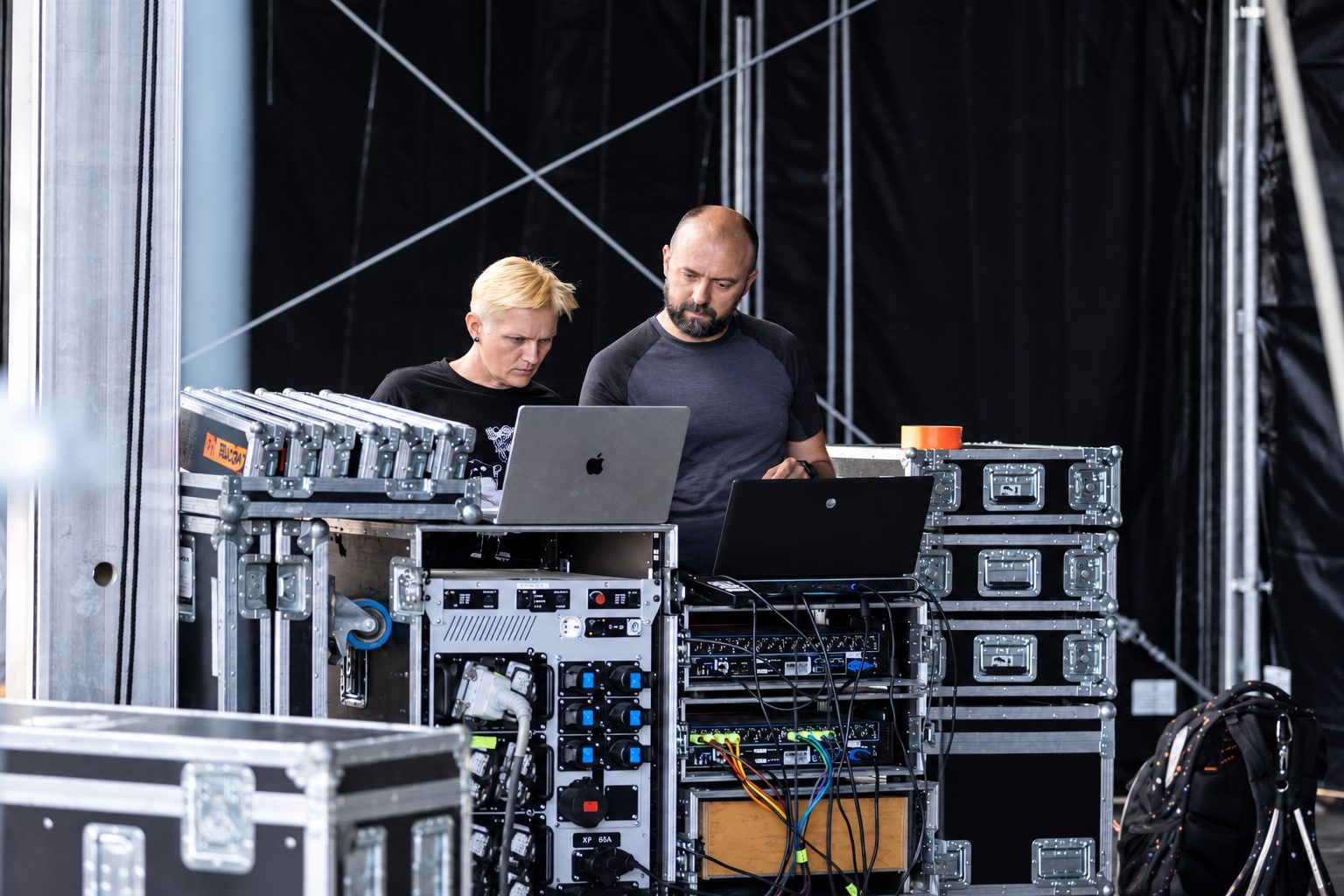 Zwei Personen prüfen an zwei Laptops auf einem Rollrack hinter der Bühne den Stand des Aufbaus