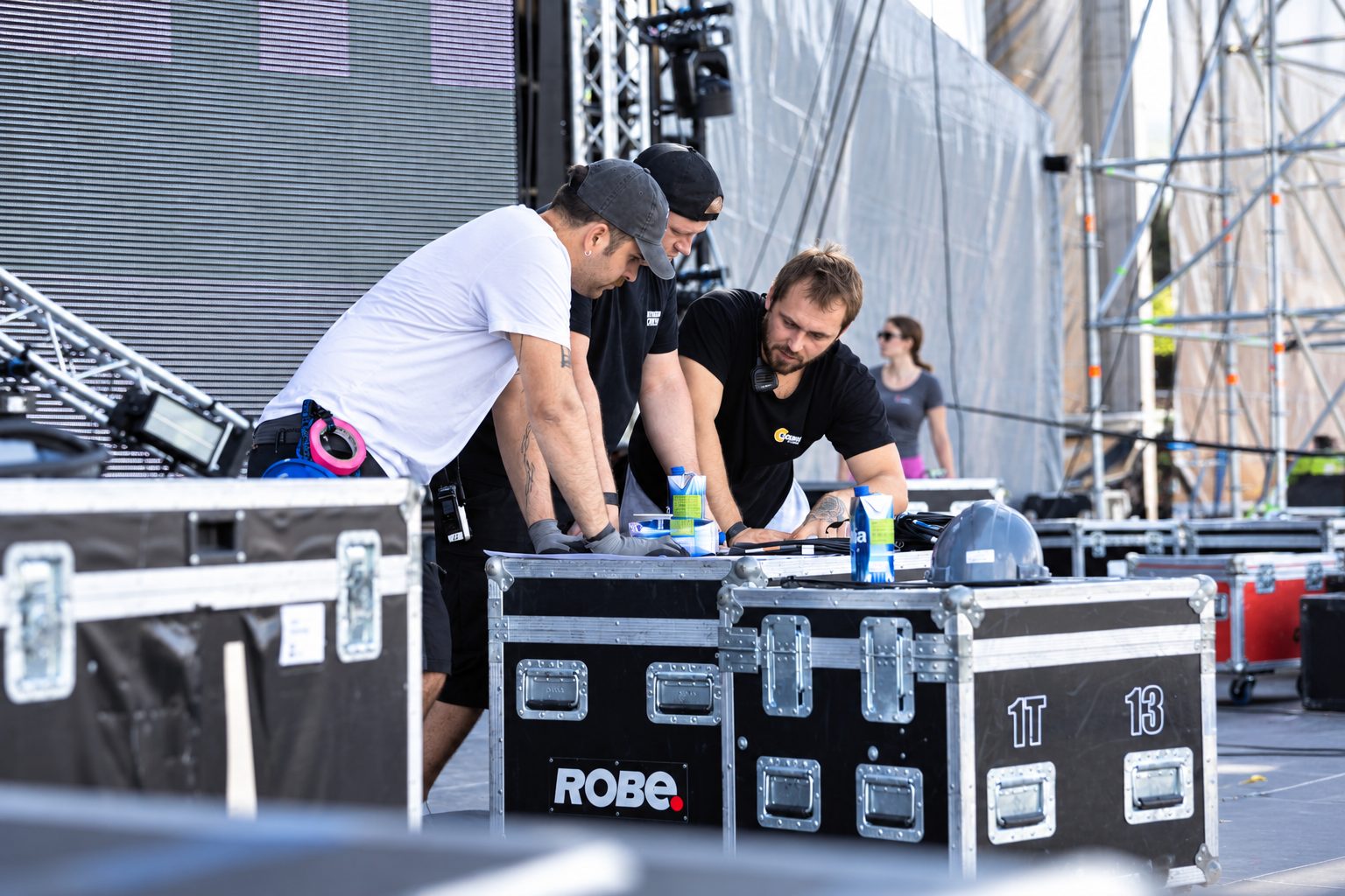 On-Site Supervisor: drei Personen besprechen Aufbauunterlagen auf einem Flightcase, eine mit Funkgerät