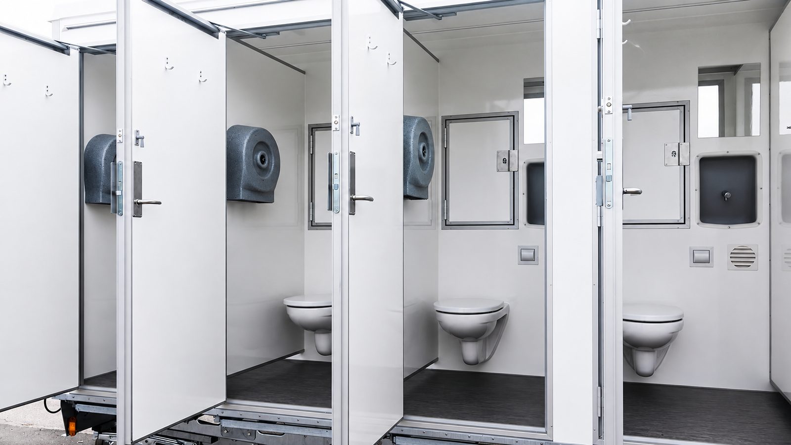Innenansicht eines Sanitäranhängers mit drei geöffneten WC-Kabinen und Papierhandtuchspendern