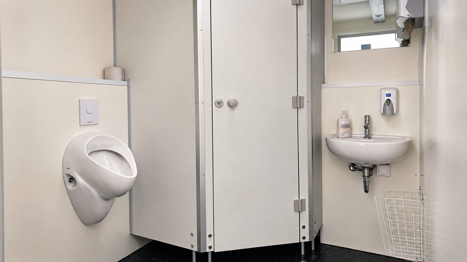 Urinal, geschlossene WC-Kabine und Waschbecken mit Seifenspender in einer mobilen Sanitäreinheit