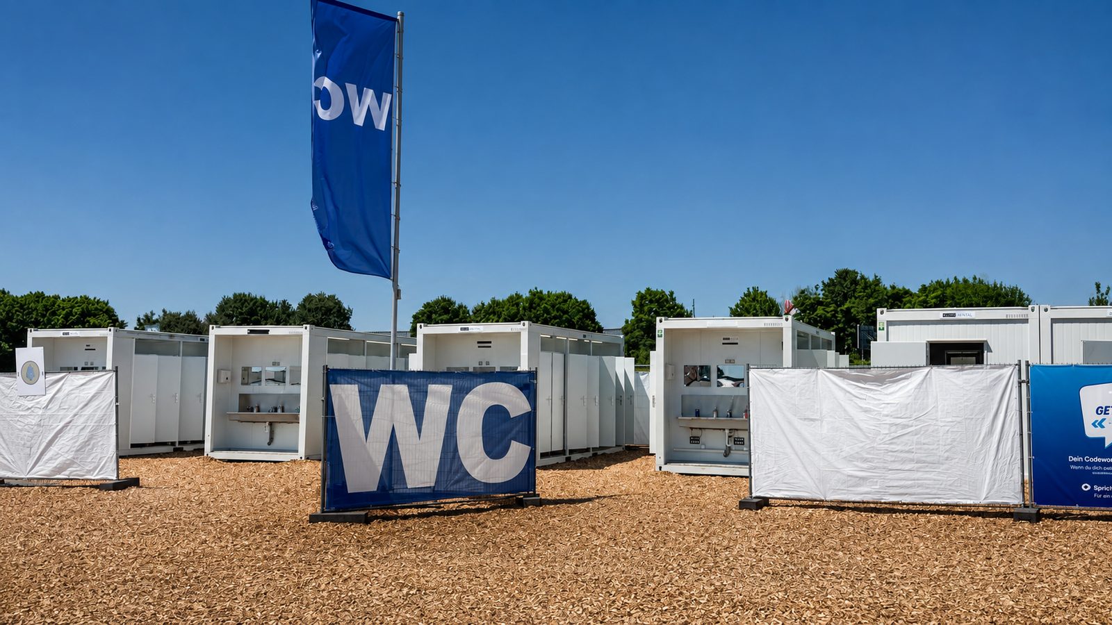 Sanitärkonzept Veranstaltung: weiße WC-Container in Reihe auf einer Hackschnitzelfläche mit WC-Banner