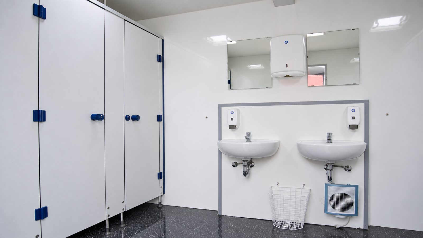 Sanitärlösungen von innen: WC-Kabinen mit blauen Beschlägen und zwei Waschbecken im Container