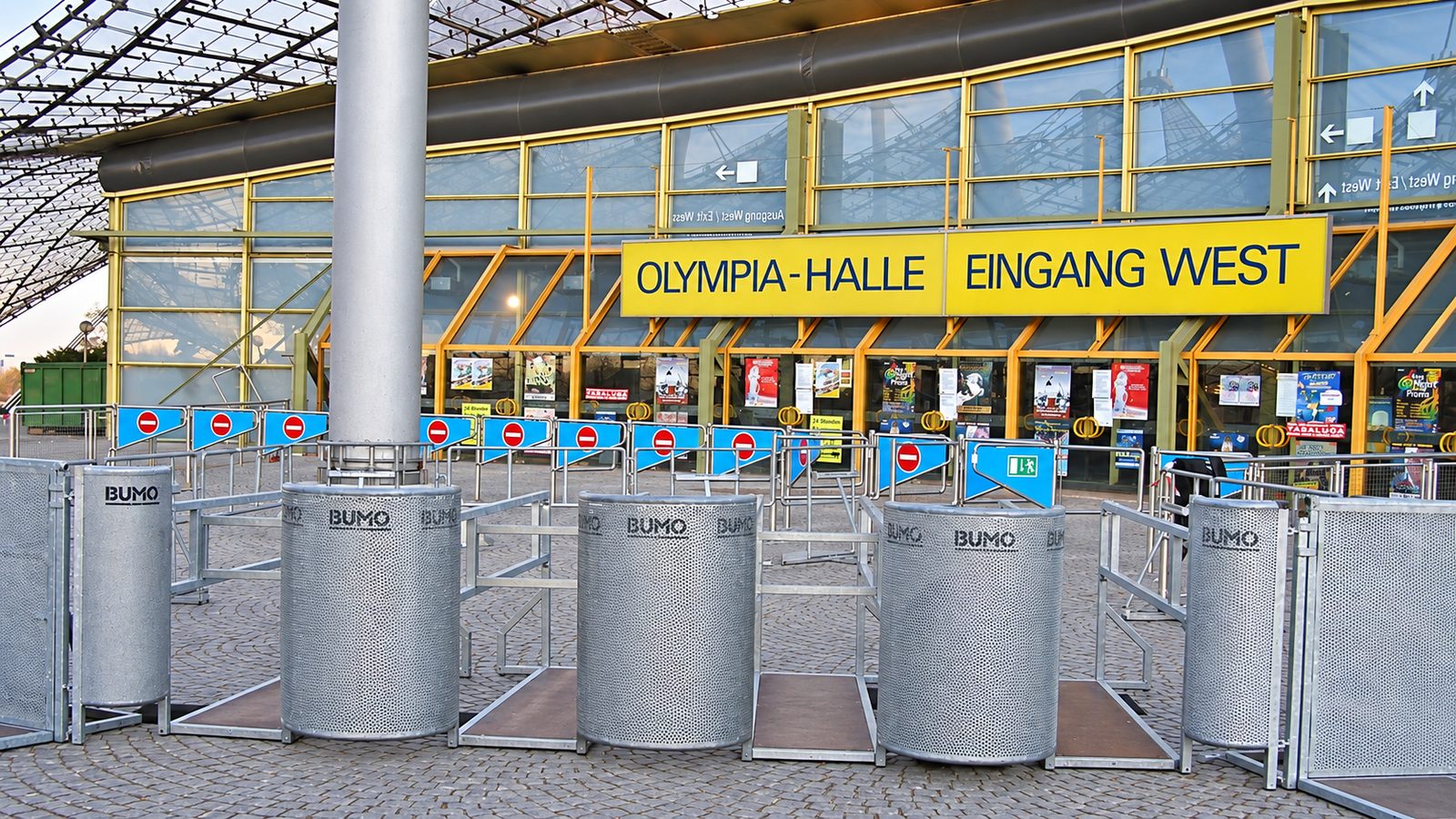 Fünf zylindrische Drehkreuz-Vereinzelungsanlagen aus verzinktem Blech vor einem Hallenzugang