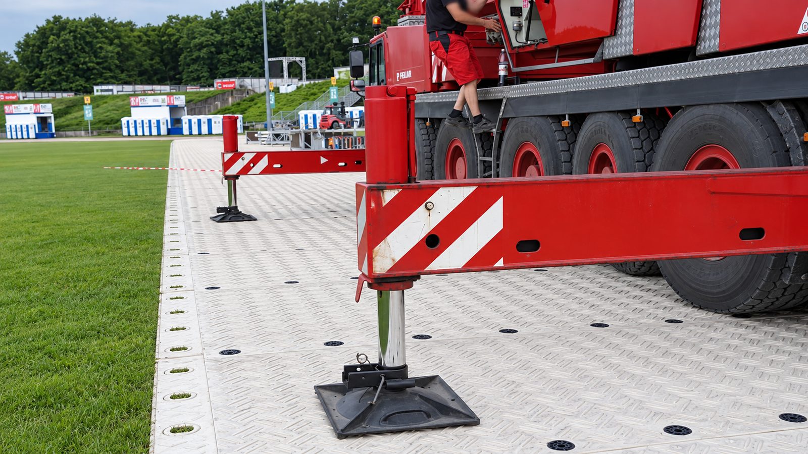 Kranabstützung auf hellgrauen Fahrplatten am Rasenrand, Stempel auf schwarzen Unterlegplatten