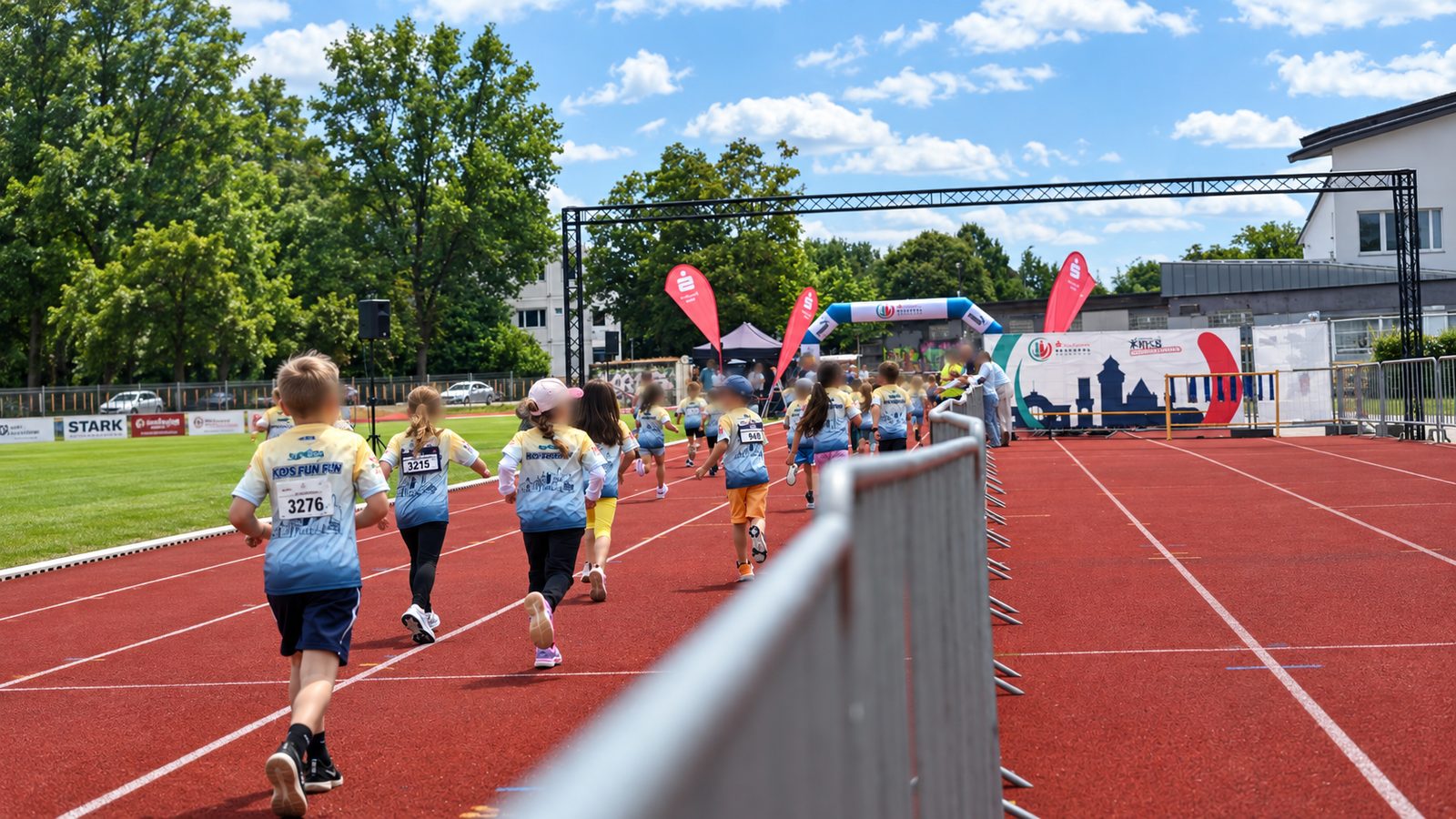 Kinderlauf auf roter Tartanbahn, seitlich eine Reihe Absperrgitter, im Hintergrund Traversenbogen und aufblasbarer Zielbogen