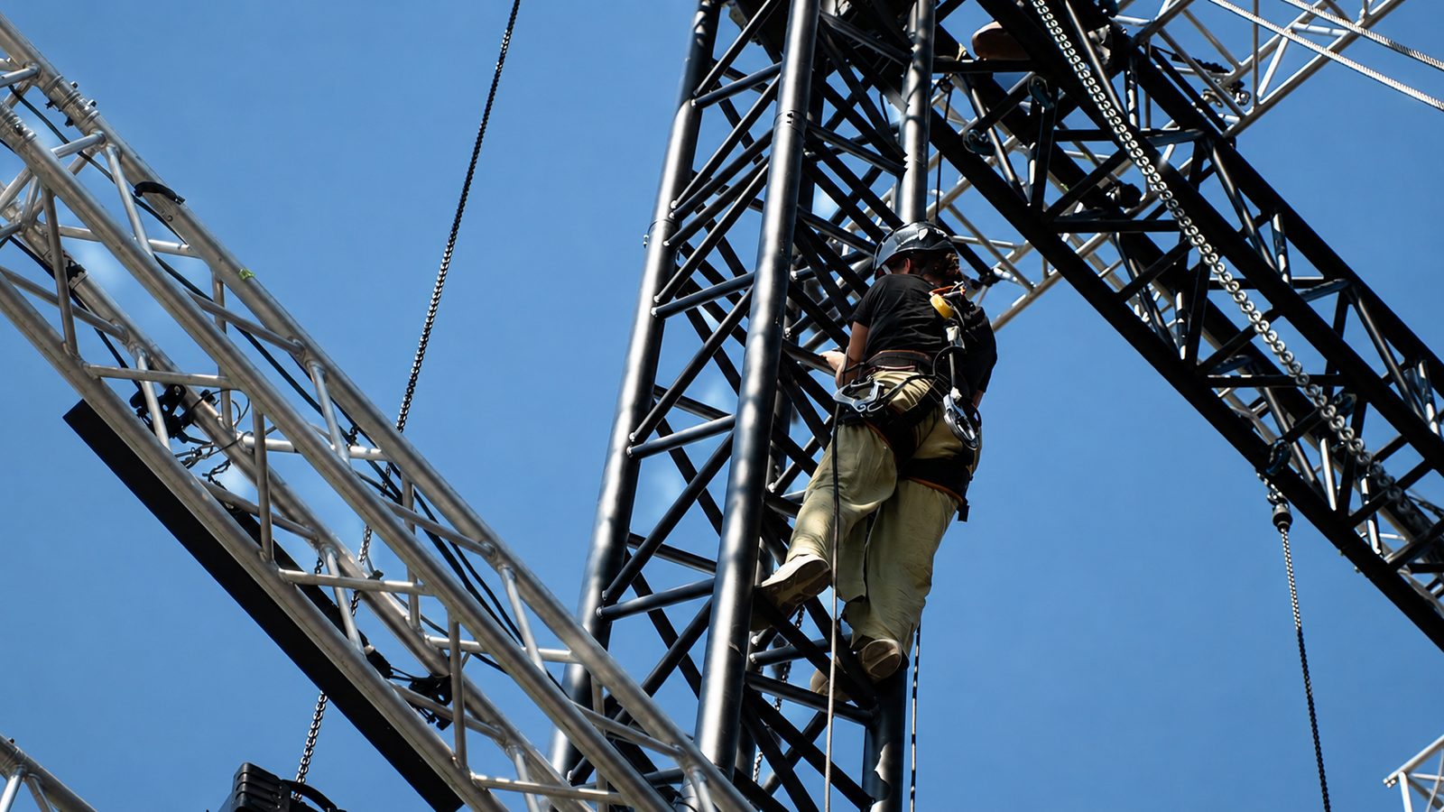 Rigger mit Helm und Klettergurt steht in einer Aluminiumtraverse vor blauem Himmel