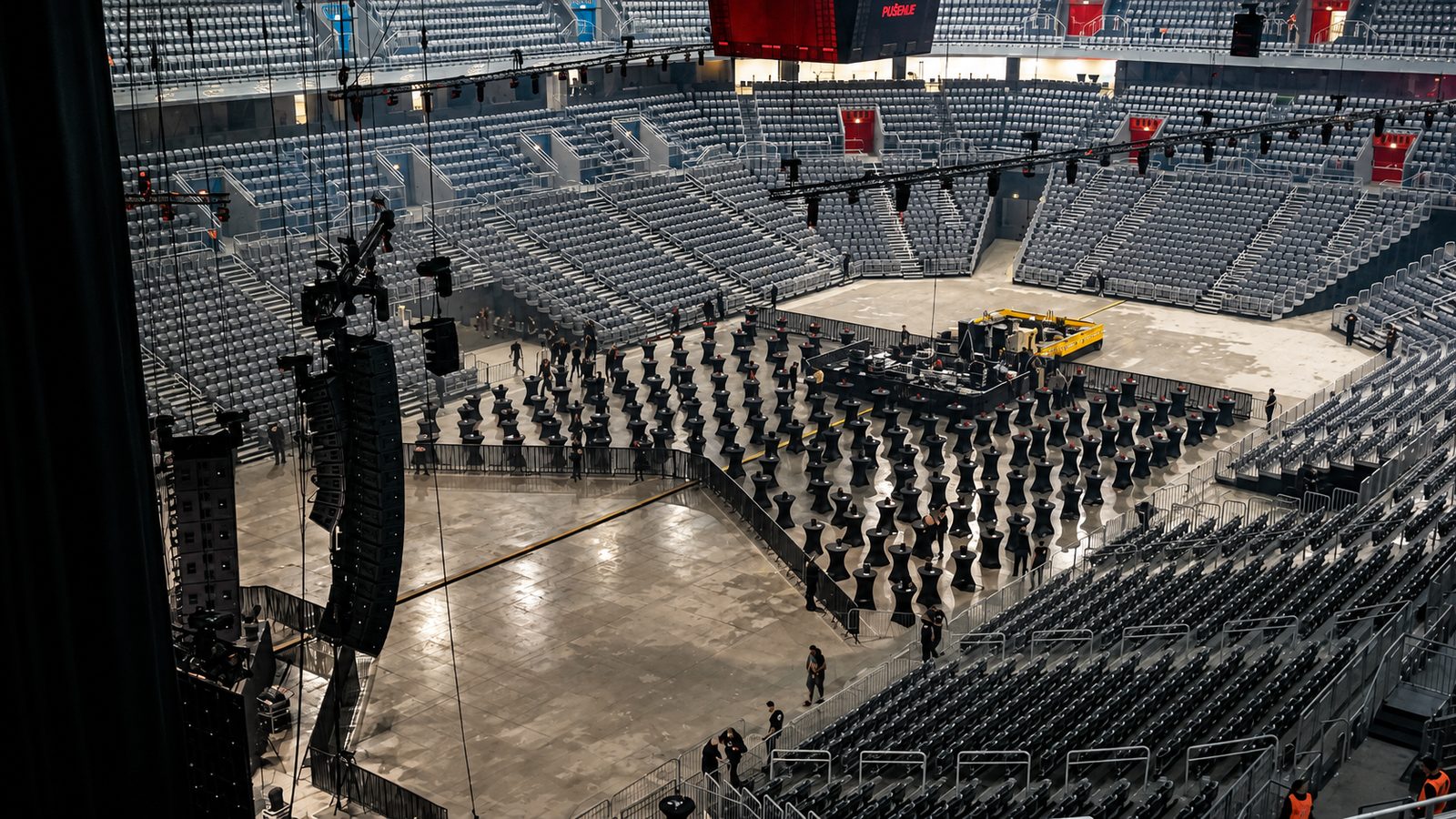 Blick vom oberen Rang einer Arena im Aufbau: feste Sitzränge, Stehtische im Innenraum, Traversen und Hebesteiger.