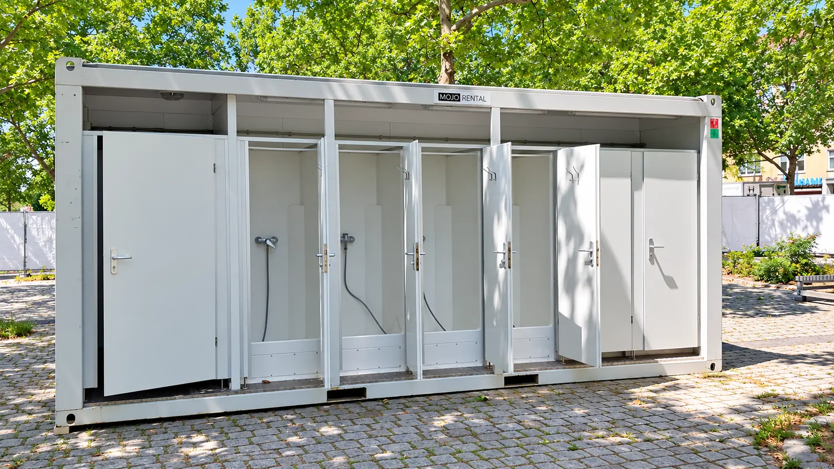 Geöffneter 20-Fuß-Duschcontainer mit mehreren Einzelduschen und Türen auf einem gepflasterten Platz unter Bäumen